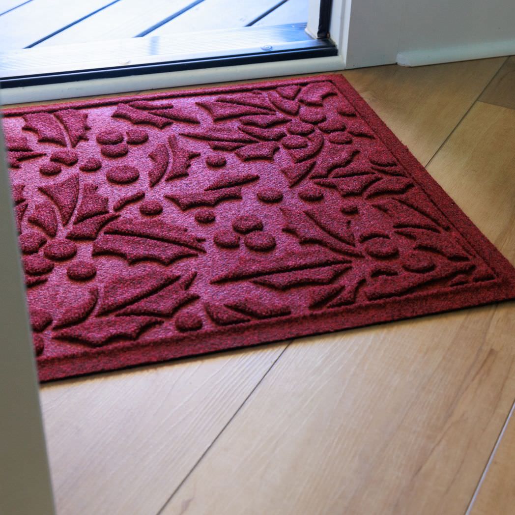 Deep red bi-level doormat with a holiday floral textured pattern on a wooden floor inside front door.