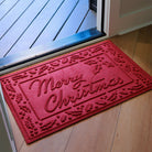 Red indoor/outdoor doormat with bi-level 'Merry Christmas' surrounded by a holly on a wooden floor inside a front door