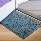 Blue indoor/outdoor doormat with snowflake pattern on a wooden floor next inside open front door.