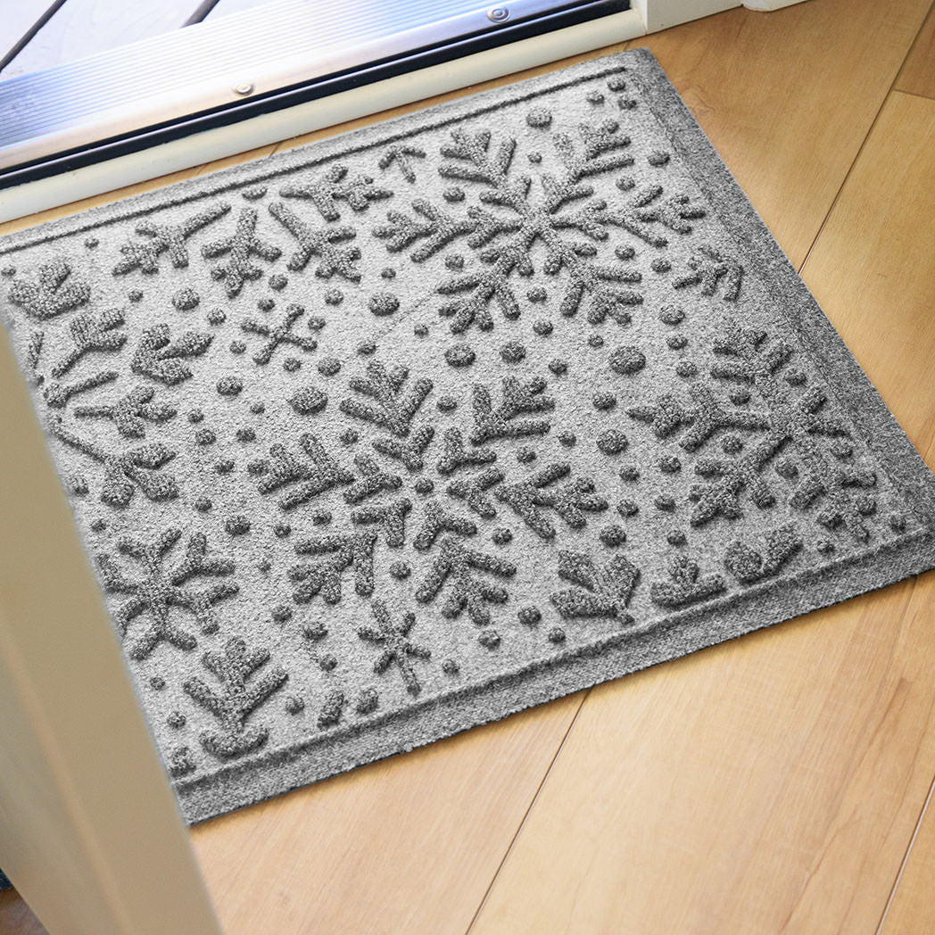 Gray doormat with bi-level snowflake pattern on a wooden floor inside front door.