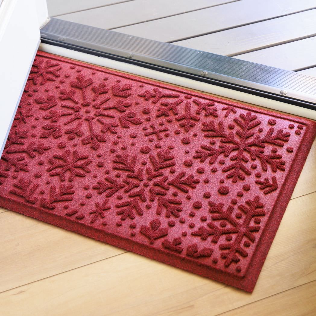 Red doormat with bi-level snowflake pattern on a wooden floor just inside open front door
