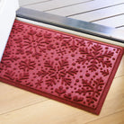 Red doormat with bi-level snowflake pattern on a wooden floor just inside open front door