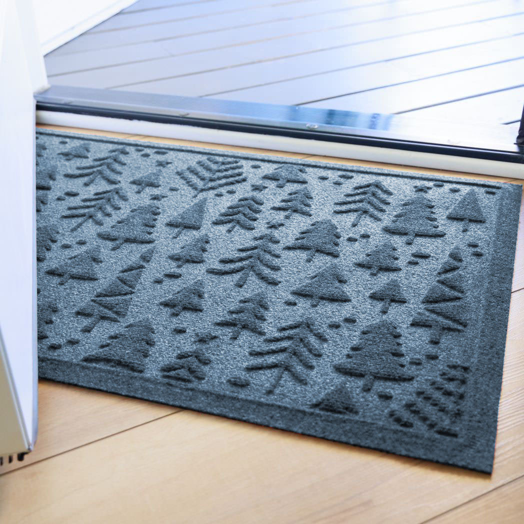 Blue with grey undertones indoor/outdoor doormat with tree pattern on a wooden floor just inside front door.