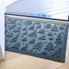 Blue with grey undertones indoor/outdoor doormat with tree pattern on a wooden floor just inside front door.