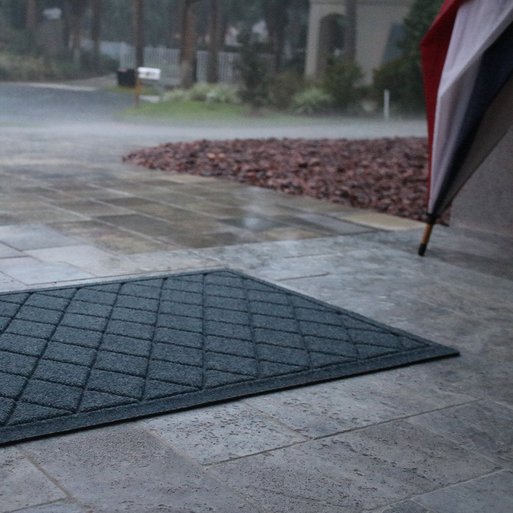 Closeup of WaterHog Argyle mat outside on a stone patio with rain falling.