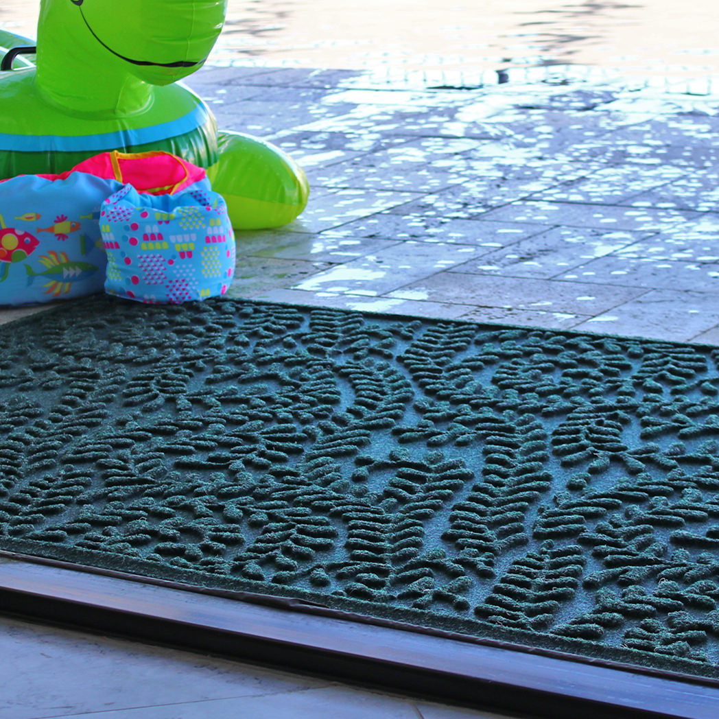 Leafy textured green doormat by a pool with inflatable toys in the background