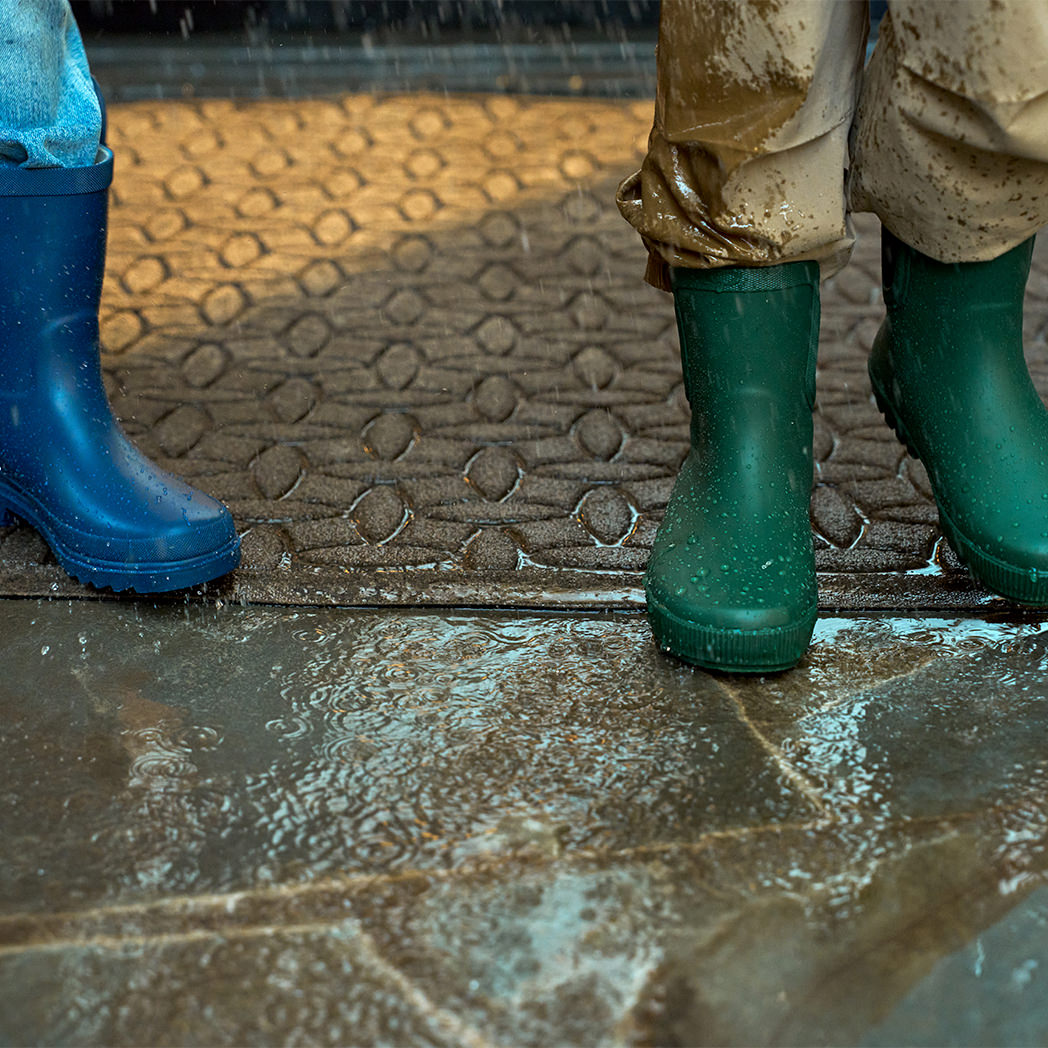 WaterHog Doormat in light tan with rain falling and kids in rainboots standing on mat.