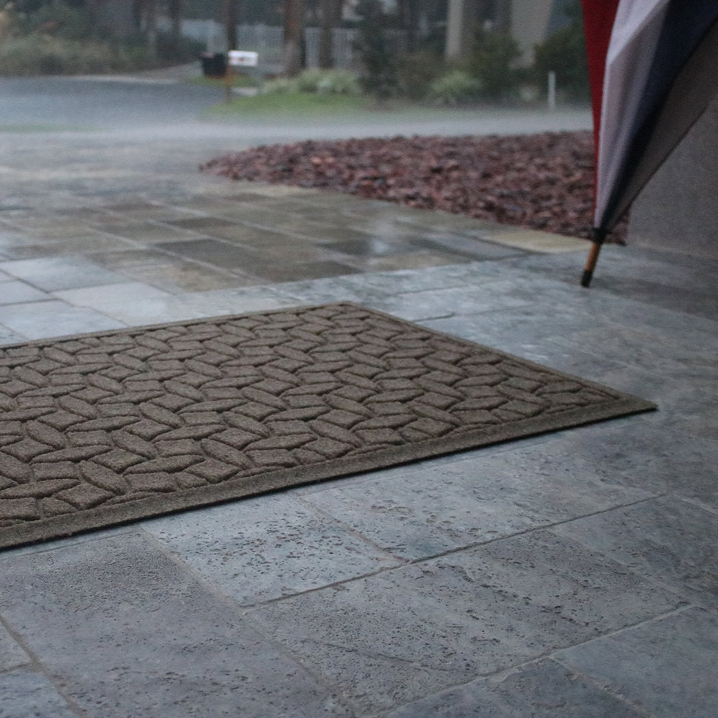 Brown WaterHog doormat on stone patio with rain falling.