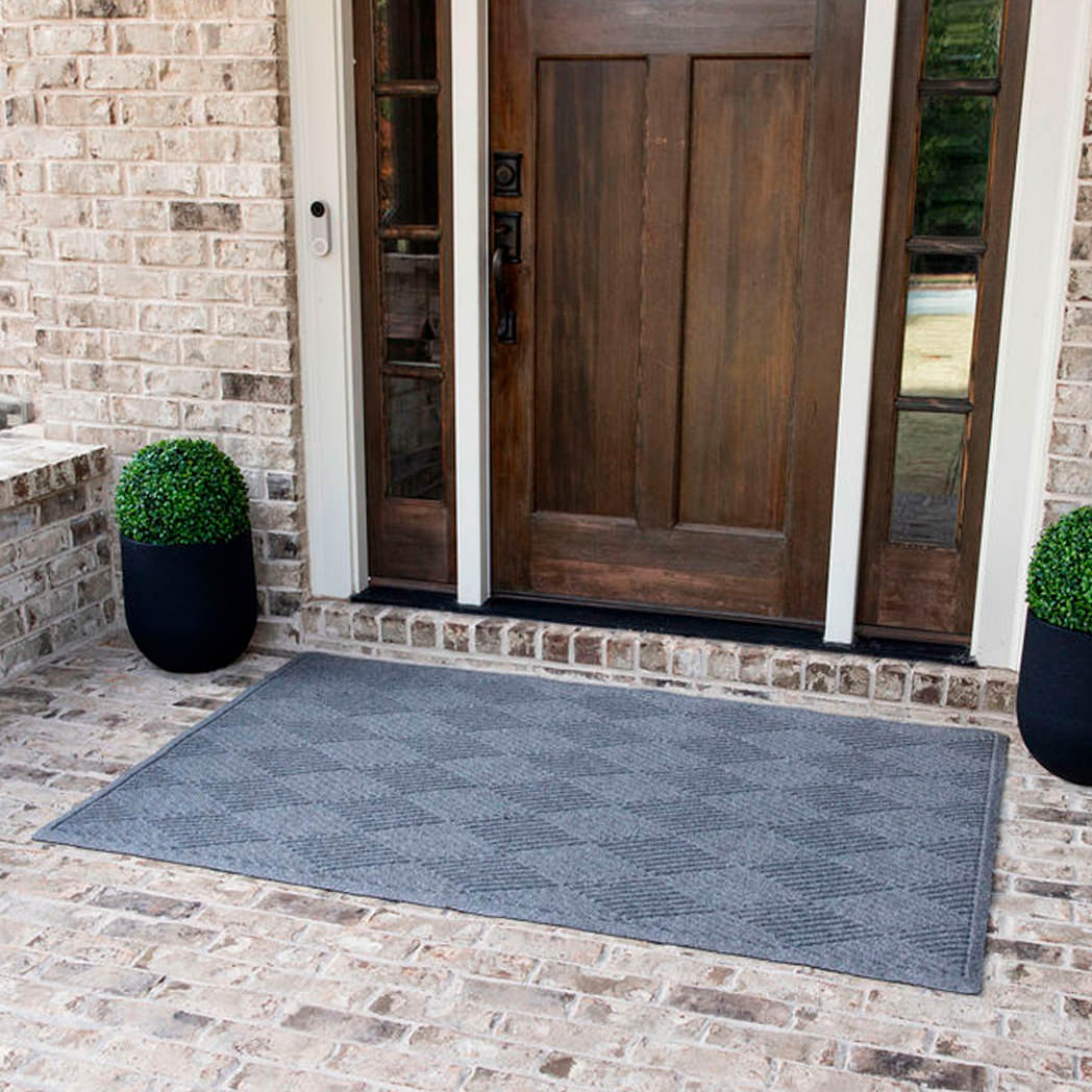 Medium grey outdoor doormat with a diamond design in the size extra-large, placed outside on brick flooring in front of a single door with sidelights.