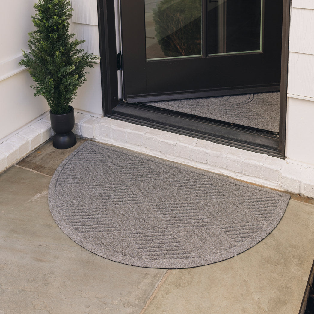 A medium grey half-round doormat, with a diamond design, is placed on tile flooring outside a single door; the door is open to show another doormat of the same color and pattern on the inside  of the door.