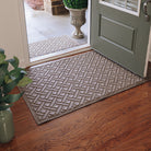 Large WaterHog Lattice indoor/outdoor mat in tan, featuring a crisscross geometric design, displayed on wood flooring in front of a single door inside, with a medium version outside on concrete.