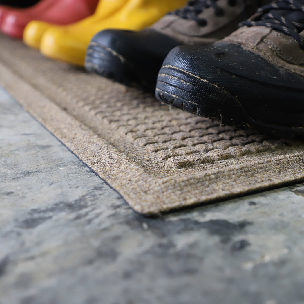 Close up image of low-profile WaterHog Squares boot tray mat with three pairs of boots sitting on top.