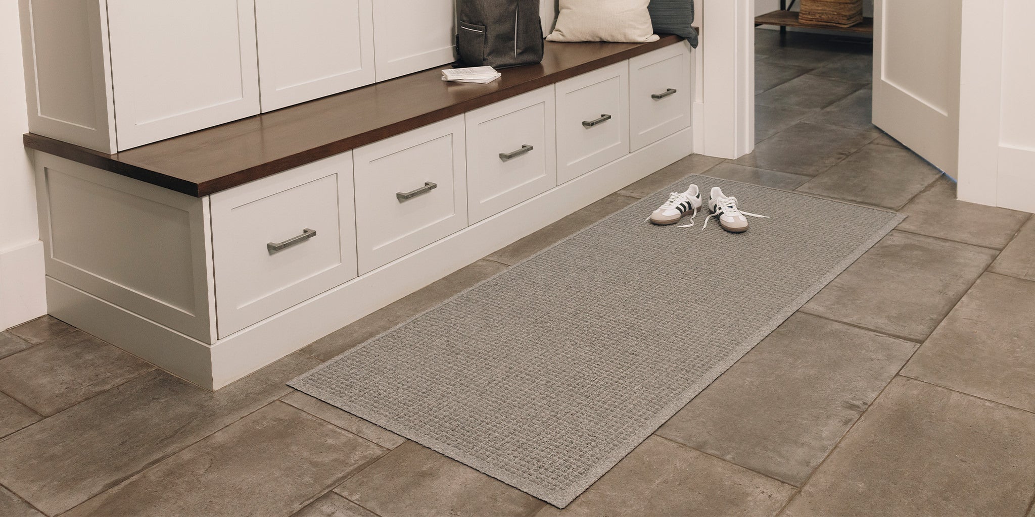 Mudroom with white cabinets, wooden bench, and a medium grey WaterHog indoor runner on stone floor