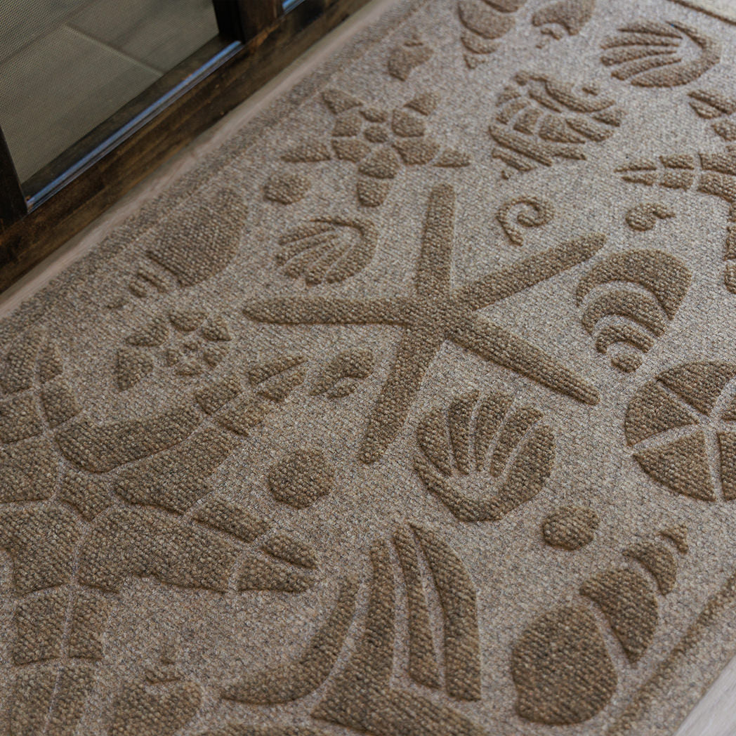 Close up on the bi-level seashell design on a camel Beachcomber mat at a front door