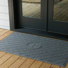 Blue WaterHog monogrammed doormat with 'P' on a wooden deck in front of a glass door.