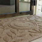 Close up of the bi-level monogrammed 'C' on a WaterHog Brittney Leaf light sand doormat at a glass door