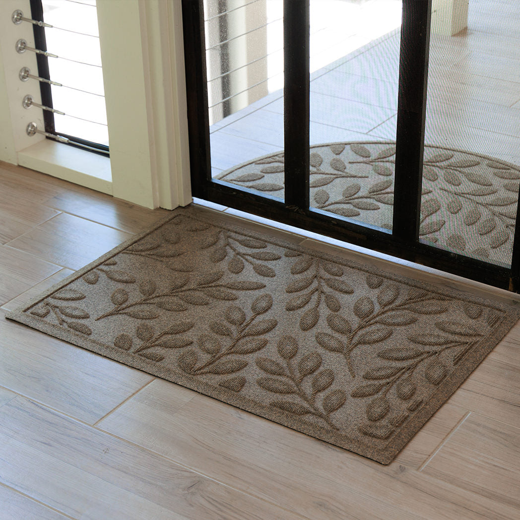 Protective doormat with leaf pattern in front of a glass door.