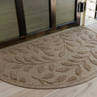 Close up of semi-circle WaterHog doormat with a bi-level leaf pattern on a wooden floor in front of a glass door.