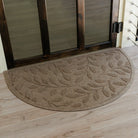 Semi-circle WaterHog doormat with leaf pattern on a wooden floor in front of a glass door.