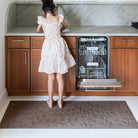 Little girl in a dress standing on a leafy-design runner with an open dishwasher in a kitchen