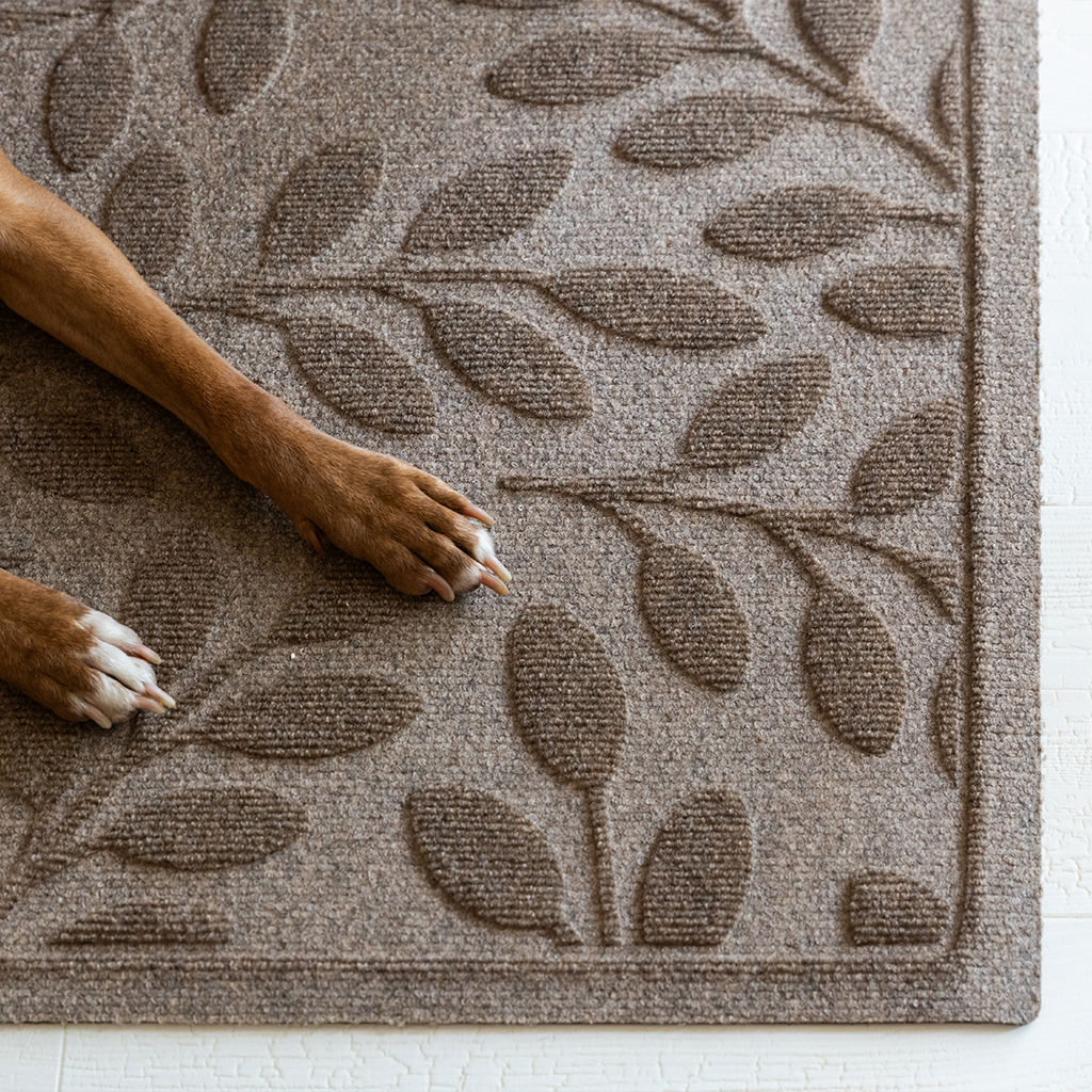 Camel colored WaterHog Runner with leaf pattern on a white floor, showing dog legs resting on top