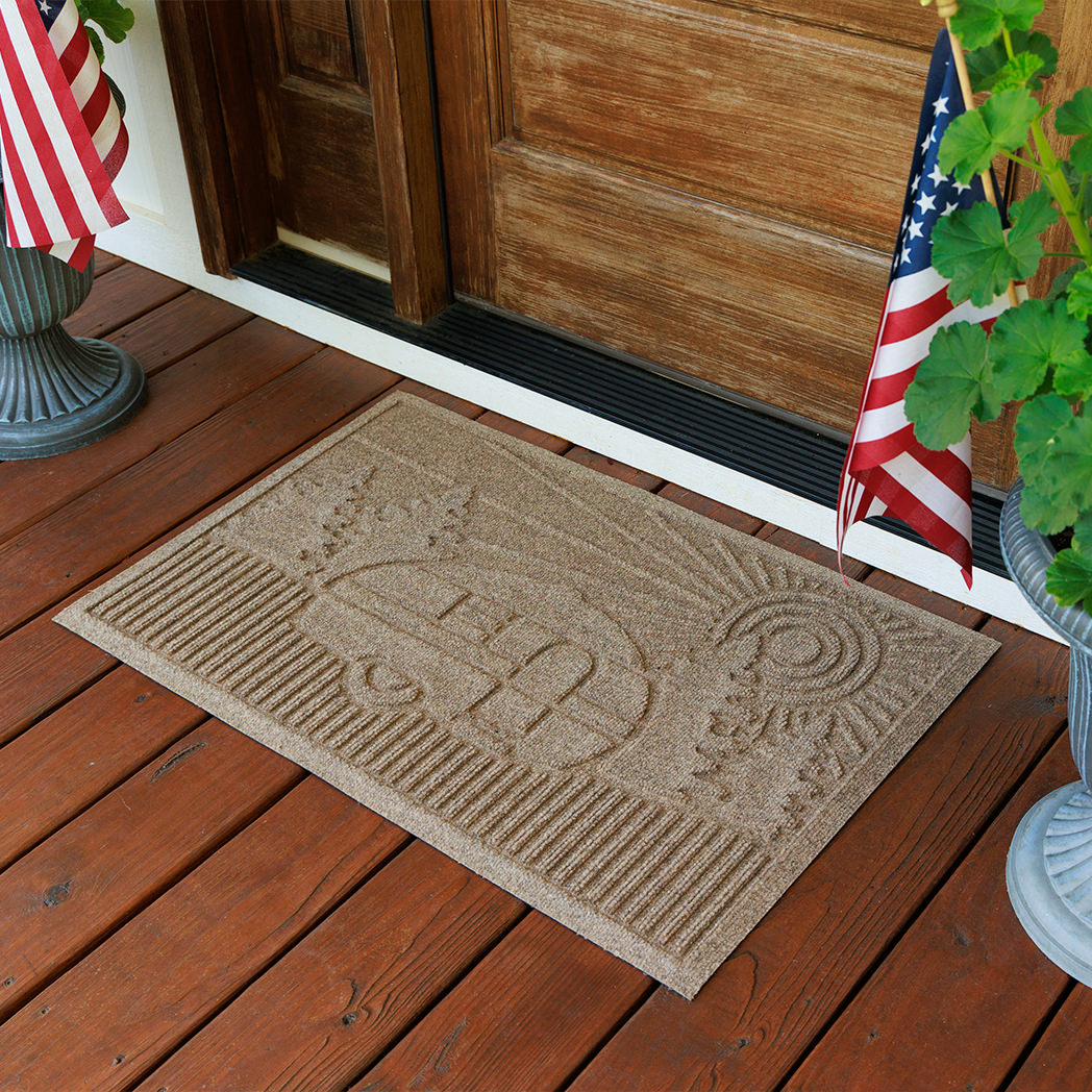 Doormat with a camper design on a wooden deck with American flags and plants.