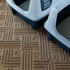 Overhead view of a tan double-size WaterHog Cat Litter Mat placed beneath two litter boxes on a hard floor. The mat’s raised paw print and line pattern are visible, designed to catch and contain litter tracked out by cats.