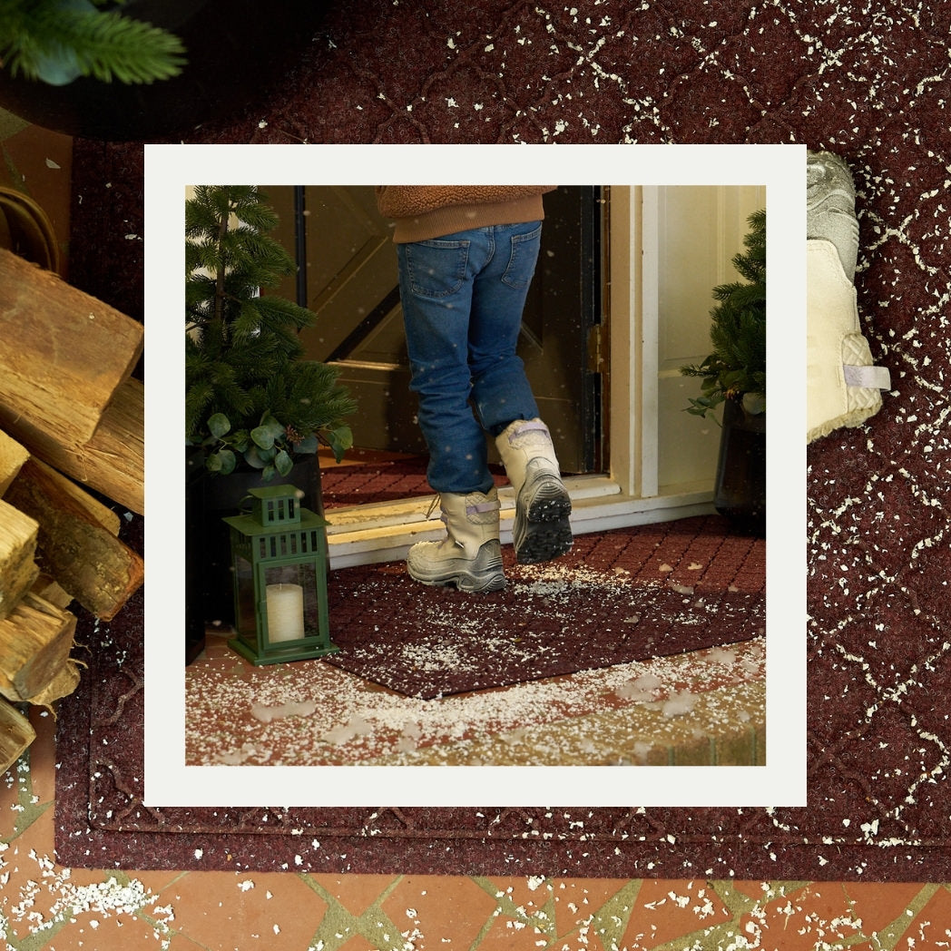 Person wearing boots stepping on a WaterHog Cordova doormat to prevent snow from coming inside