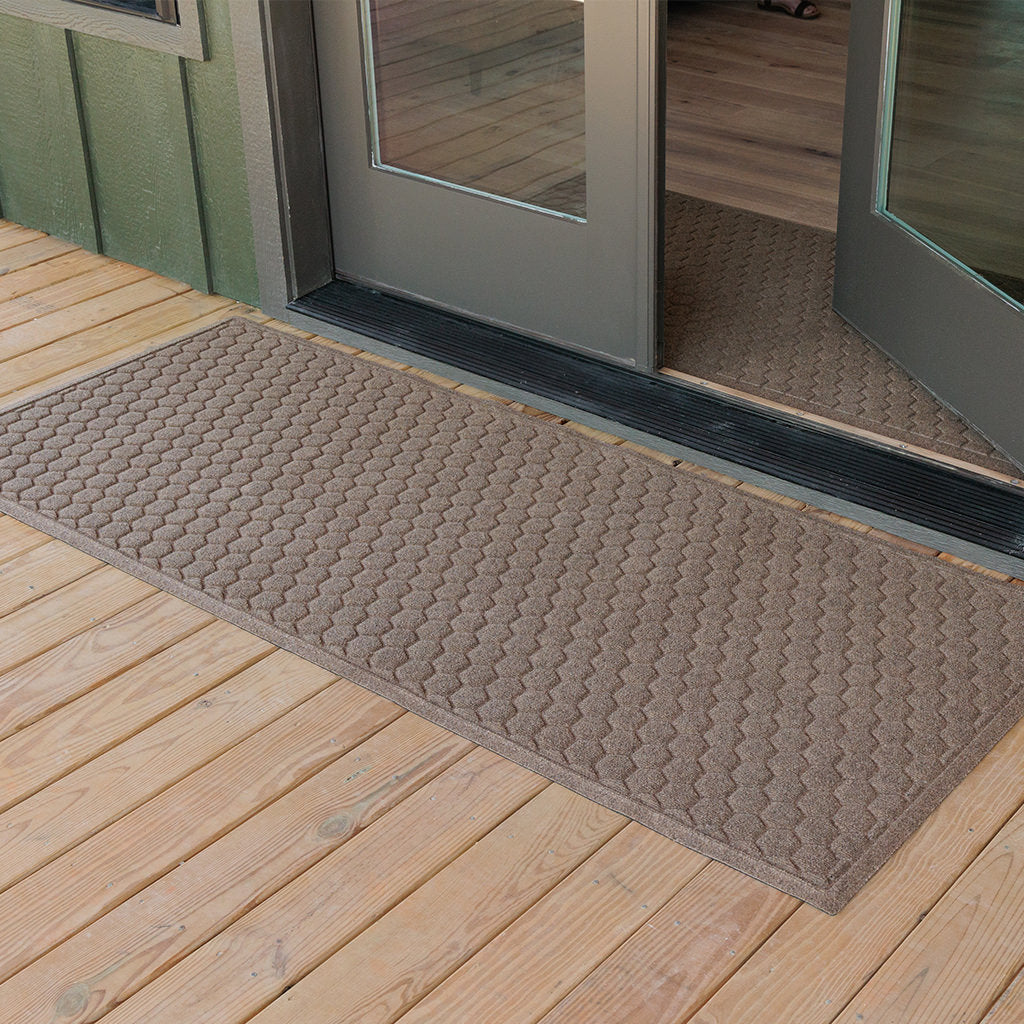 A WaterHog Honeycomb Runner mat at the front door of a green cabin house