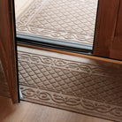 Tan WaterHog Tristan runner placed just inside a wood entryway and matching doormat outside the door, both featuring a raised diamond-and-scroll bi-level surface made of durable PET fibers that trap dirt and moisture on light wood flooring.