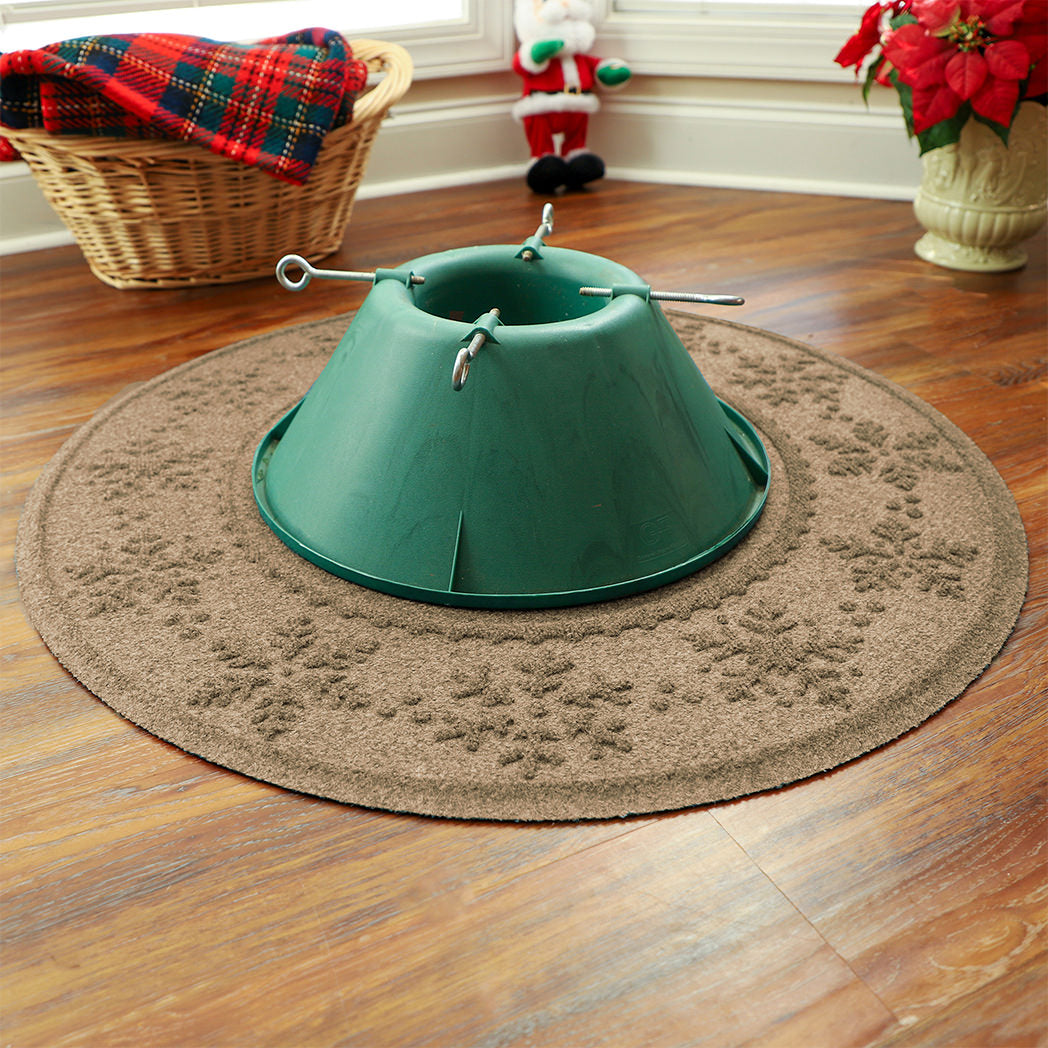 Green Christmas tree stand on a tan WaterHog Holiday Tree Skirt with holiday decorations in the background.