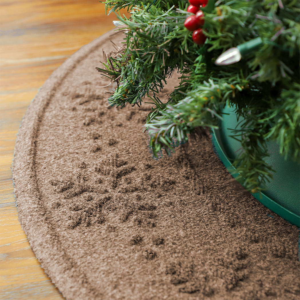 Brown doormat with a snowflake design under a potted Christmas tree on a wooden floor.