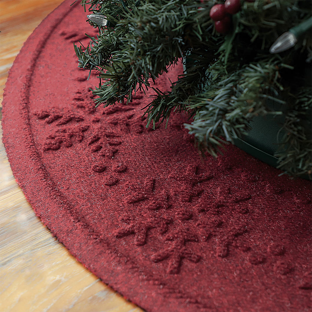 A deep wine-red snowflake tree skirt mat with a Christmas tree on a wood floor