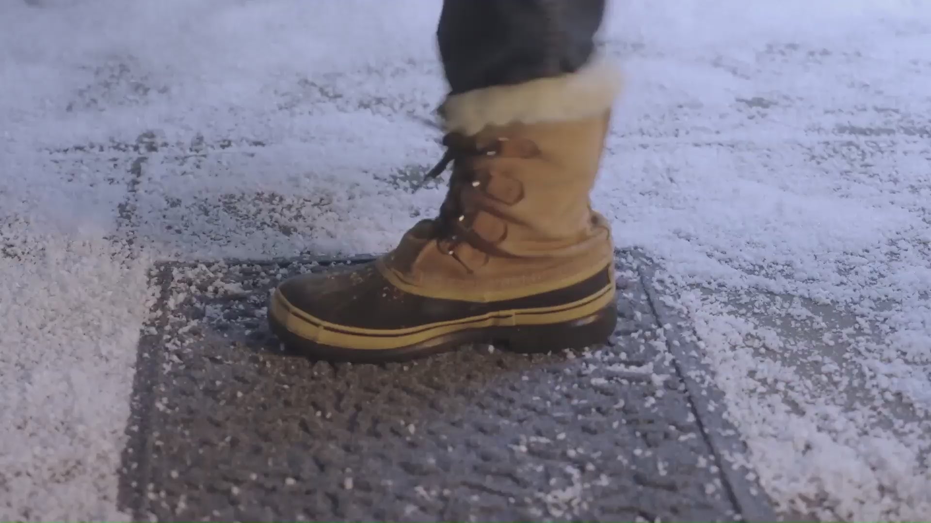 Various peoples shoes walking and scraping snow off their boots and a red and blue snowflake-design holiday doormat