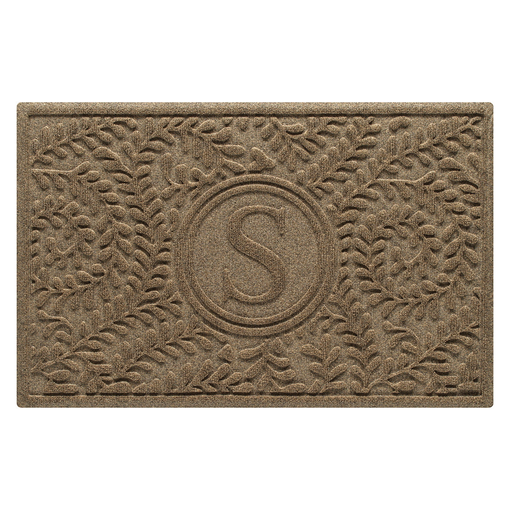 Overhead of a WaterHog Boxwood medium-sized monogram doormat in a light tan curling botanical, bi-level design.