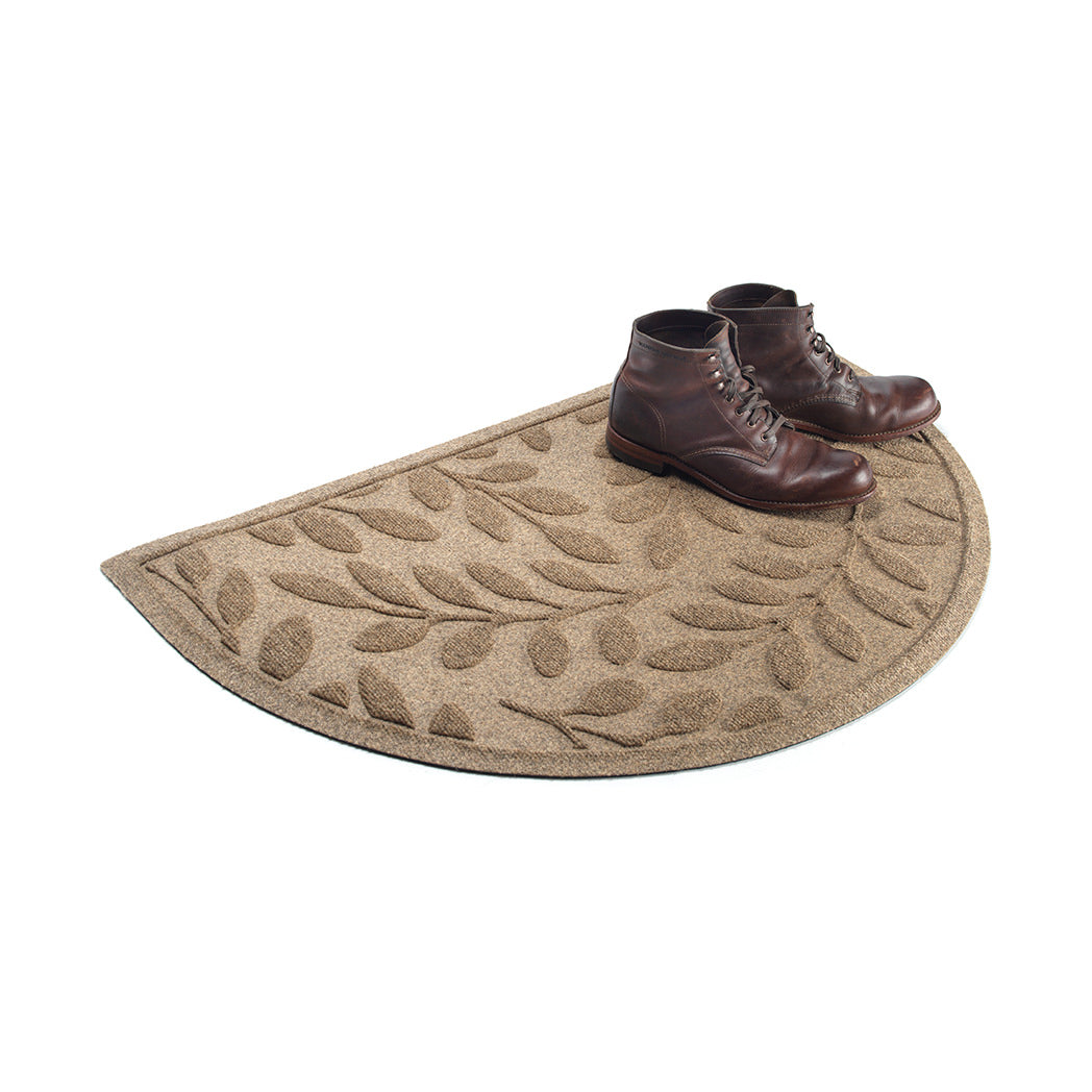 Beautiful tan/beige WaterHog half-round doormat with botanical leaf design with a pair of brown lace-up boot sitting on mat.