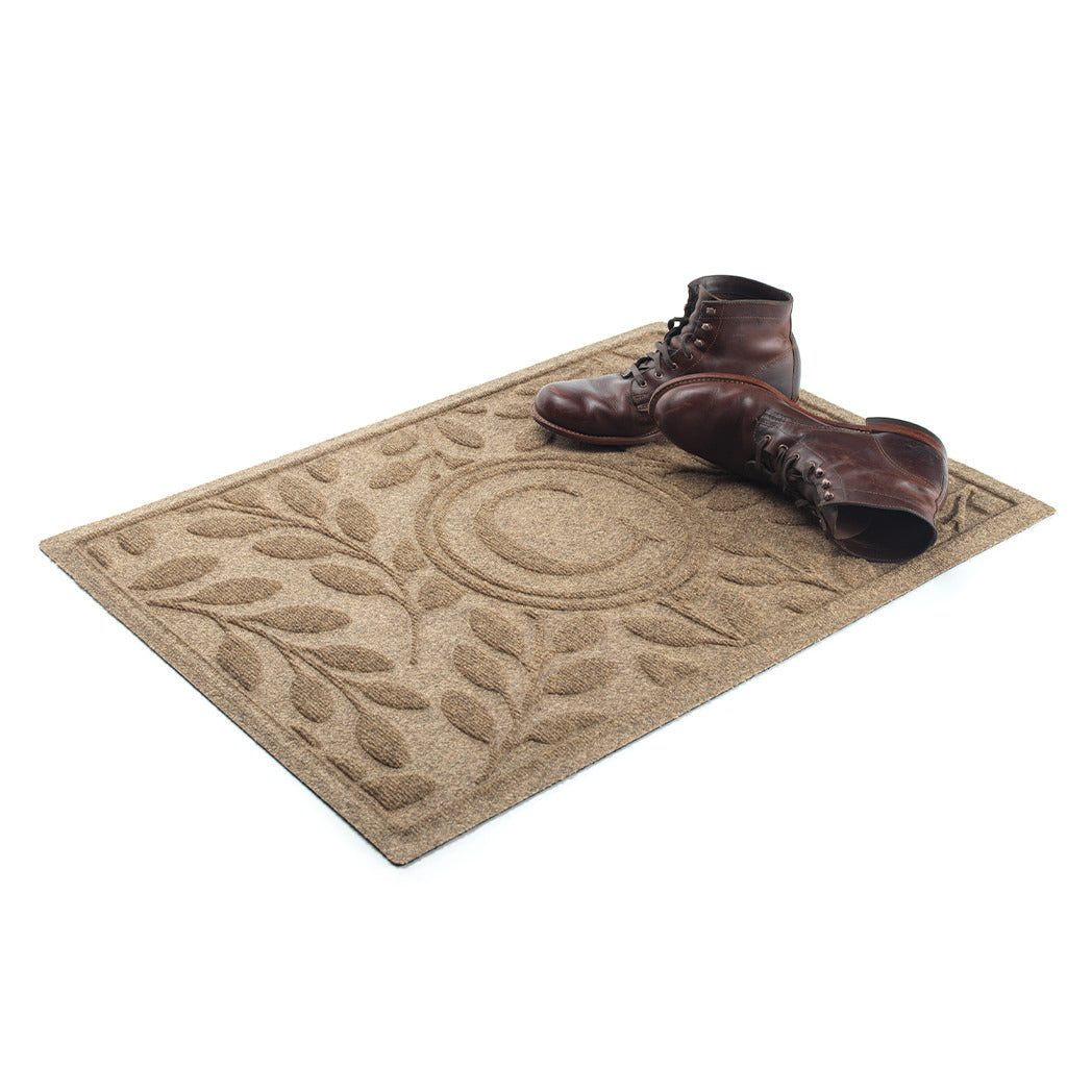 tan/beige WaterHog Brittney leaf doormat monogrammed with a letter in the center with a pair of lace-up brown boots sitting on top.