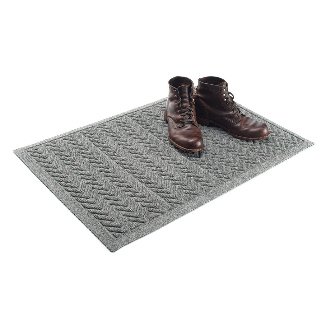 Modern WaterHog indoor/outdoor doormat in a medium grey color with a zig-zag v-shaped pattern with a pair of brown leather boots placed on top.