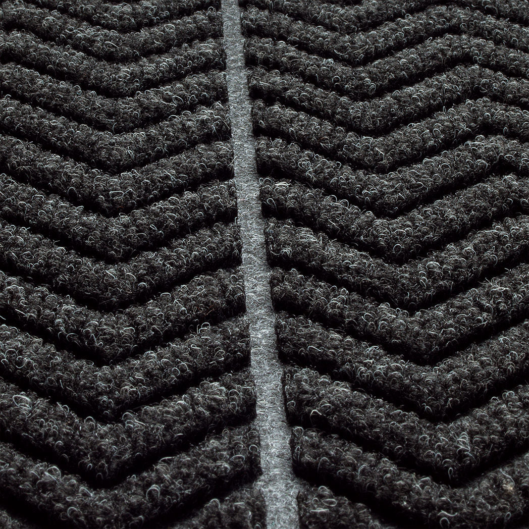 Zoomed in view of WaterHog Chevron doormat's surface detailing the bi-level recycled PET surface in fiber colors black and grey.