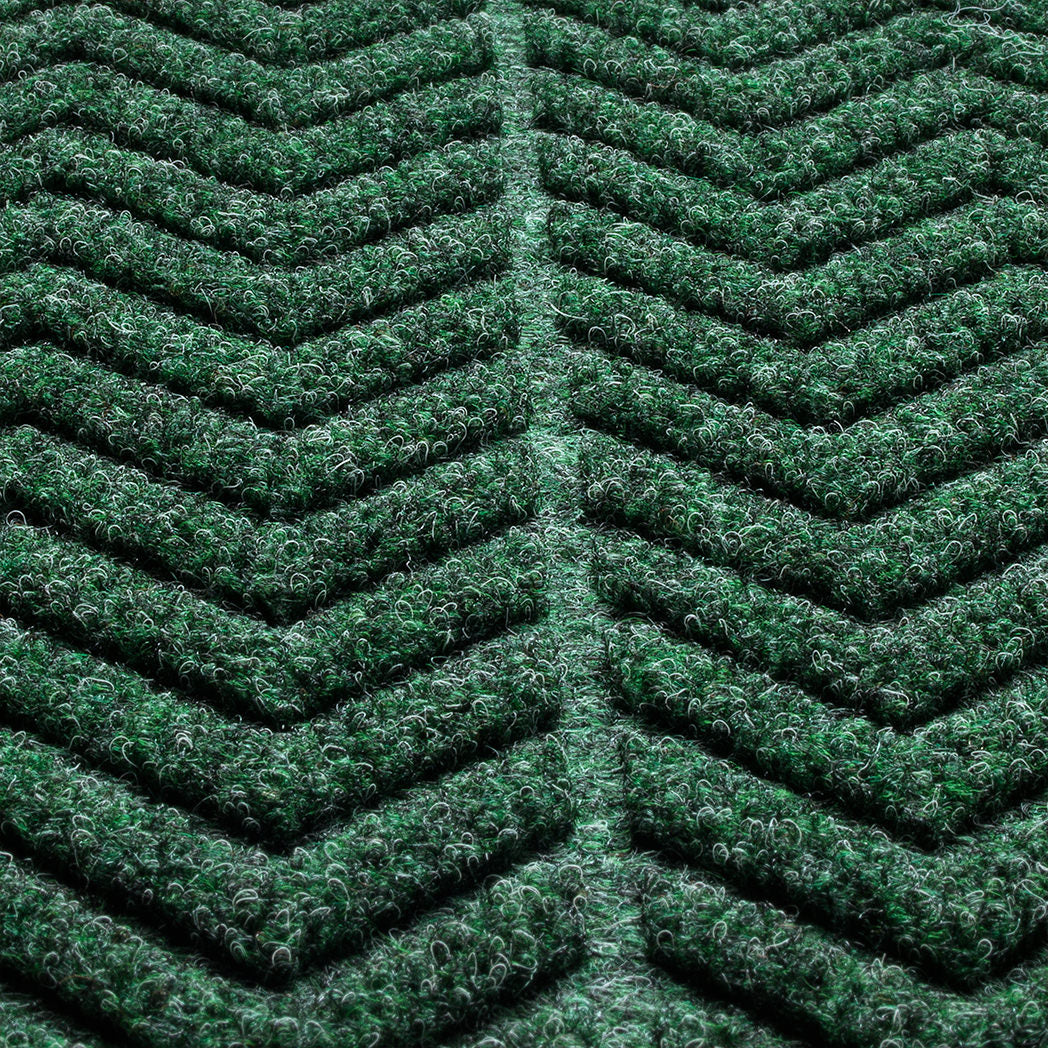 Close-up of a textured WaterHog doormat with a  chevron pattern made from a fibrous material consisting of colors green with some black and grey. The raised sections of the pattern create a three-dimensional effect designed for effective dirt and moisture trapping.