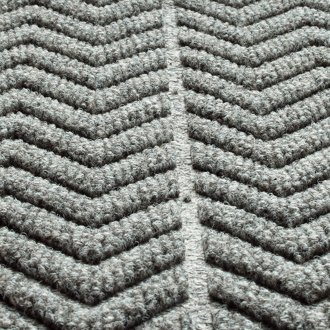 Close-up of a textured WaterHog doormat with a chevron pattern made from a fibrous material consisting of colors light grey and dark grey. The raised sections of the pattern create a three-dimensional effect designed for effective dirt and moisture trapping.