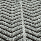 Close-up of a textured WaterHog doormat with a  chevron pattern made from a fibrous material consisting of colors light grey and dark grey. The raised sections of the pattern create a three-dimensional effect designed for effective dirt and moisture trapping.