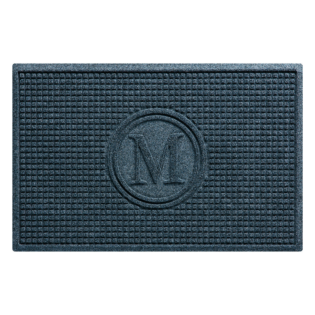 Overhead of a WaterHog Squares outdoor doormat monogrammed with a serif M, encased by two circles surrounded by a uniform grid design in a relaxed blue color; an American-made mat.