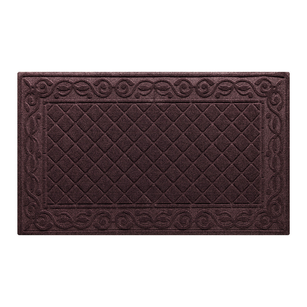 An overhead view of a large, dusty red Tristan all-weather doormat, which features an ornate scrollwork pattern that borders the classic, squared-off diamonds pattern in the center; all in a bi-level design and with a water dam border.