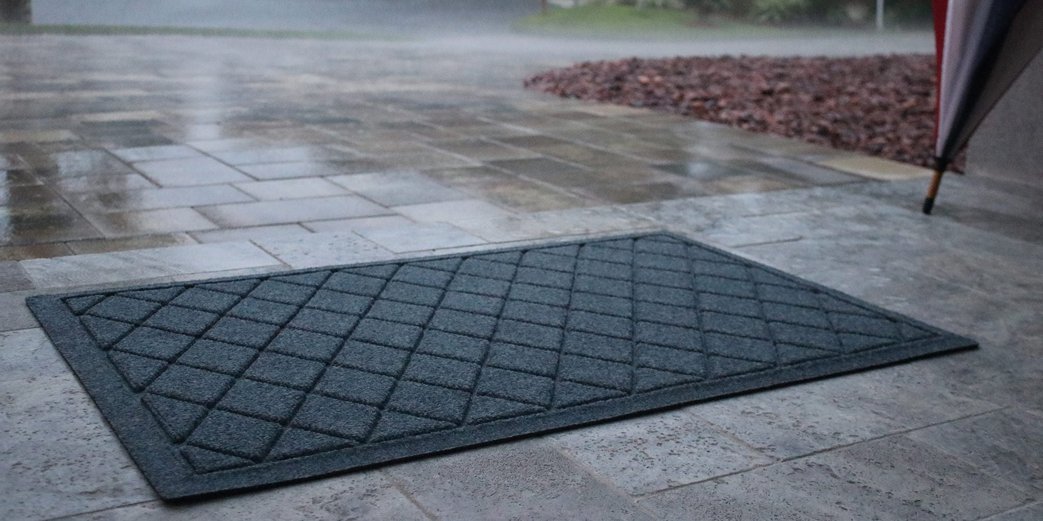 Rain falling on a stone patio in front of a beautiful, low-profile WaterHog doormat.