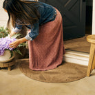 A quality WaterHog luxury half-round-doormat in light brown camel at a beautiful doorway with a woman standing on the mat, tending to plants.