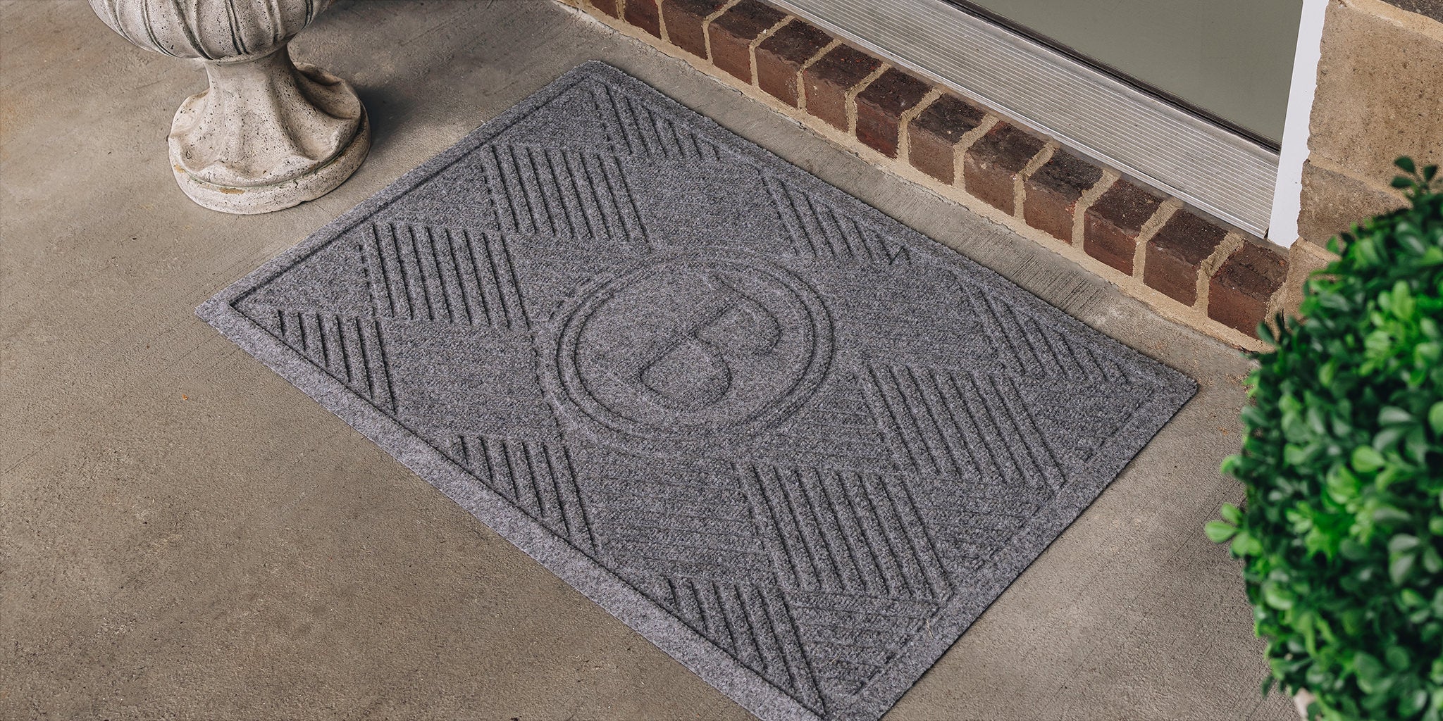 Gray personalized WaterHog Diamonds doormat, initialed with P, at a single green door on concrete ground.