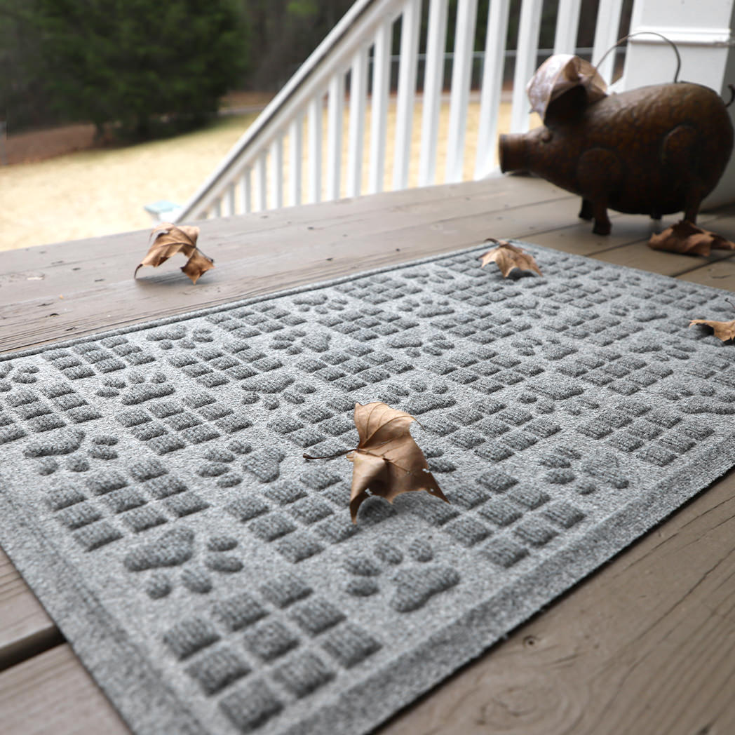 WaterHog Dog Paws Squares is a pet-themed mat shown placed on a front porch with leaves tracked on top.