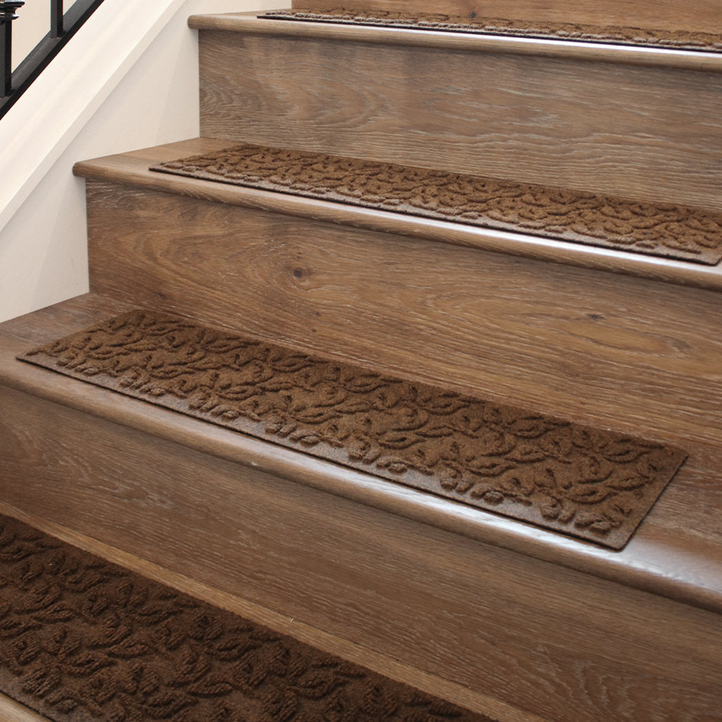 WaterHog Stair Treads in Dogwood Leaf pattern in a dark brown color placed indoors on wooden stairs.