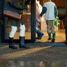 Large WaterHog Doormat in front of sliding glass doors. Rain is falling and three people in rubber boots are walking inside across the mat. 